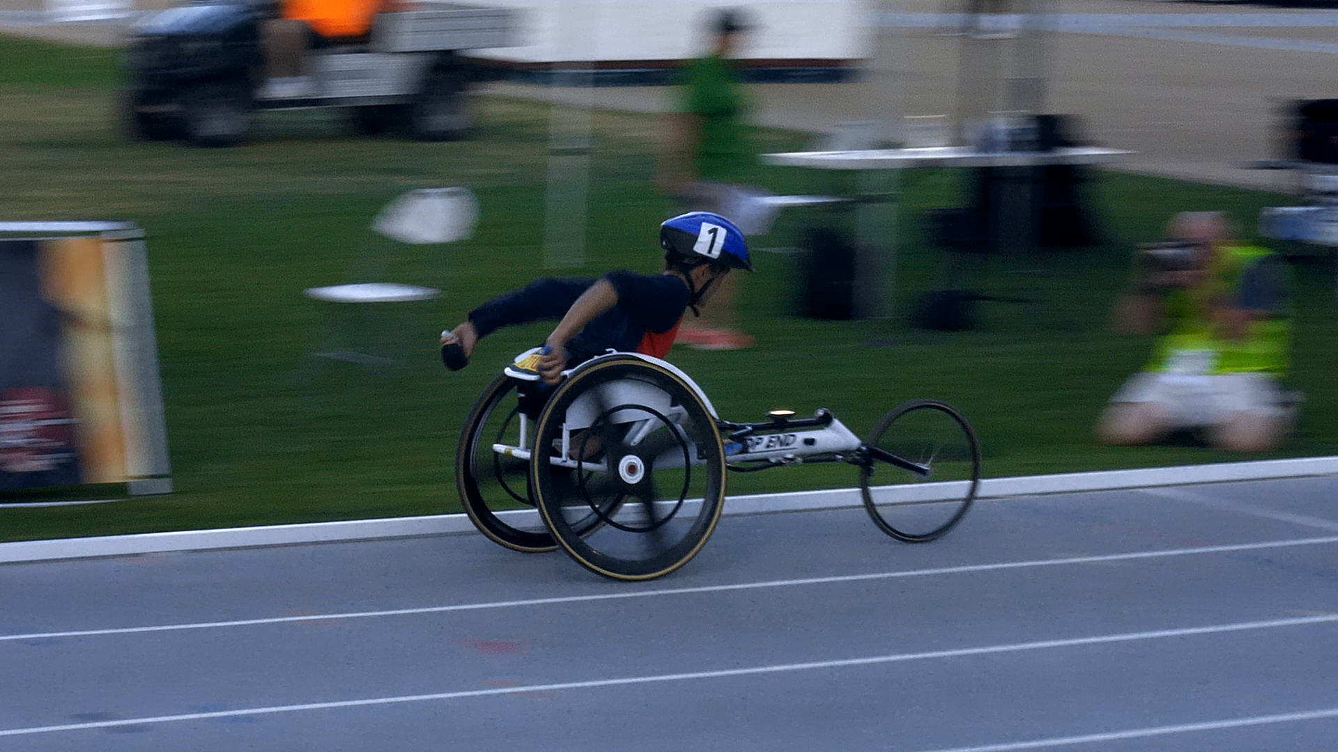 Let ’Em Play – Michael Seo Wheelchair Race Michael Seo propelling a racing wheelchair along a blue track.