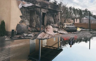 Damaged buildings at Yasnohorodka ecopark reflected in a pool of water.