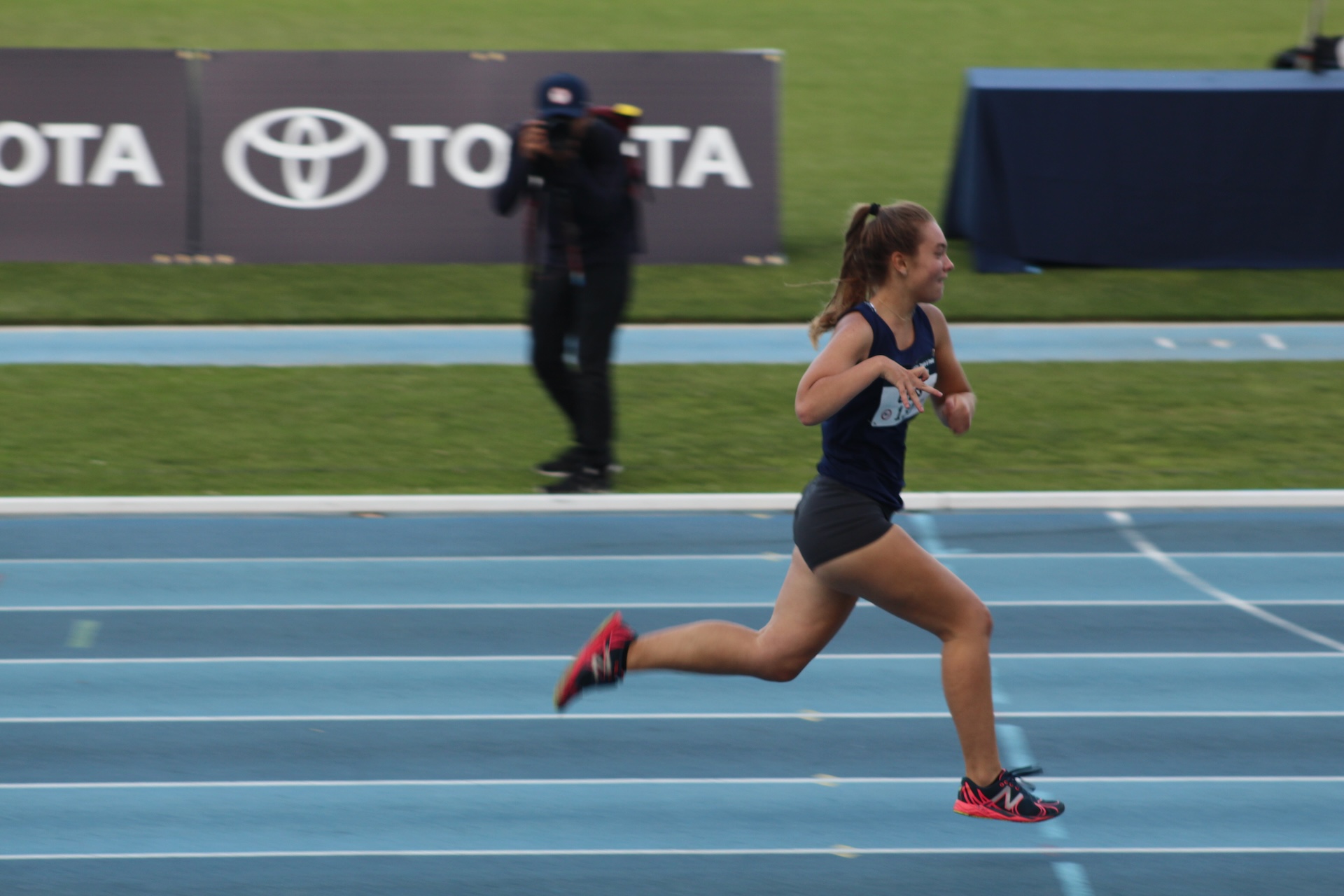 Let ’Em Play – Michelle Cross Running Michelle Cross running on a blue track during a track and field race.