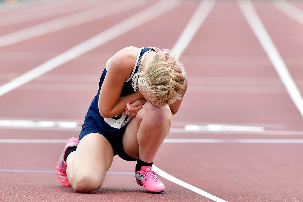 Let ’Em Play – Teylor Becher on the Track Teylor Becher kneeling on a running track with her head bowed.